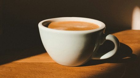 Image of a white coffee cup filled with coffee kept on a brown wall