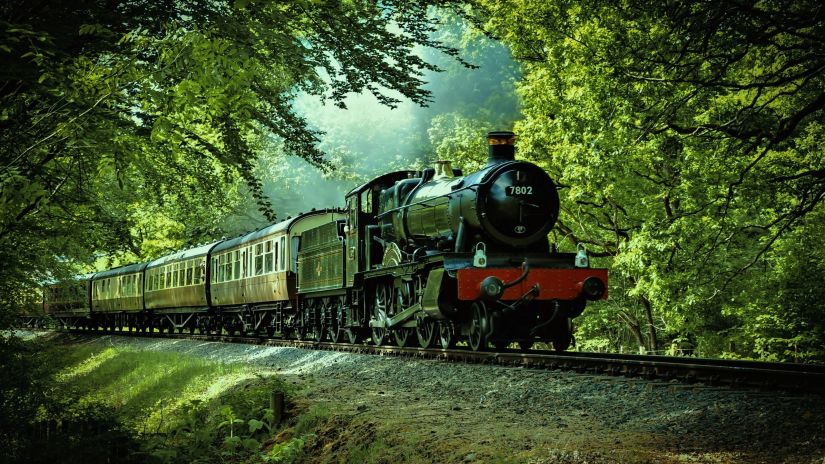 A black and red train moving along on the tracks with nature surrounding it