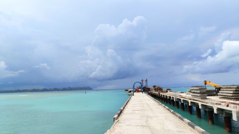 a clean blue ocean at Havelock island, new name being Swaraj Dweep, was shot from afar where we can see the sky and ocean meeting at the horizon and a pathway on the left