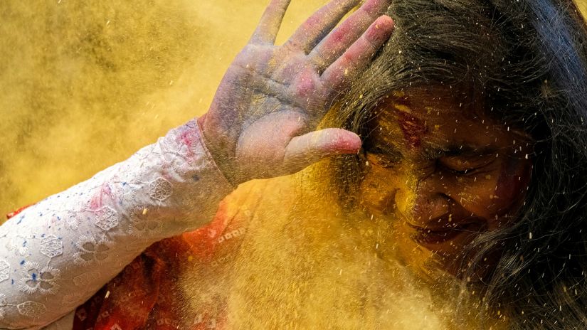 a girl unsuccessfully shielding herself from holi colours with her palms over her face