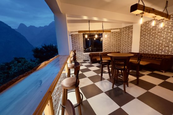 alt-text Bar seating area with wooden chairs and black and white floors in The Bourbon Club N Lounge at The Tattva Boutique Resort, Joshimath