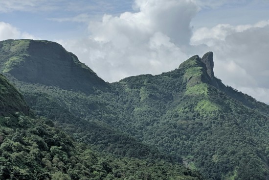 alt-text  A majestic green mountain peak under a partly cloudy sky, showcasing the lush vegetation of the steep slopes.