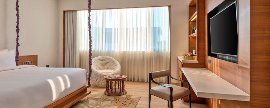 alt-text Hotel room in South Goa with wooden interiors, furniture and a white bed that offers in-room massage