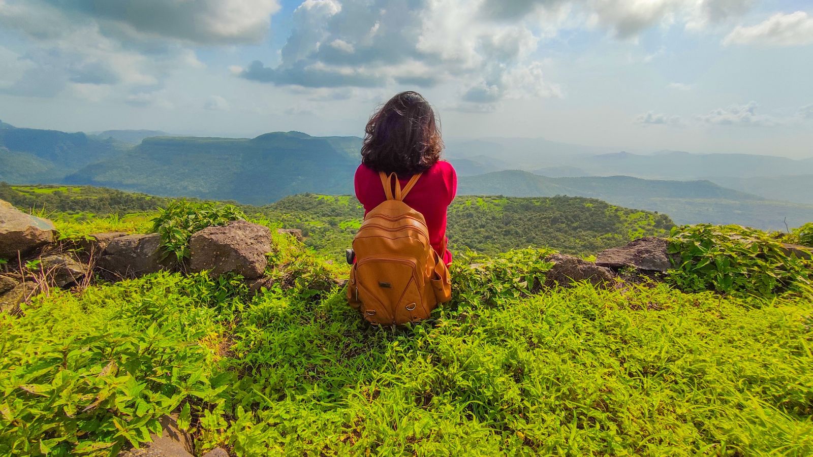 a female with a backpack sitting on top of a cliff in Lonavala