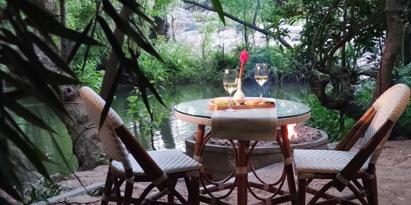 Outdoor dining setup by a river at dusk-Amanvana Spa Resort, Coorg - Luxury Resort