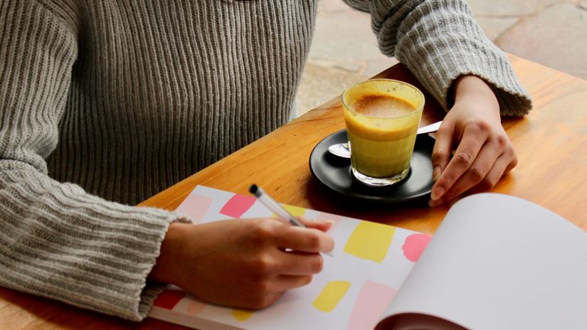 a person sitting on a chair and planning while writing on a book with a coffee on the table