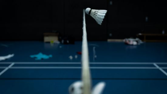 An overview of a badminton court with a cock flying just above the net