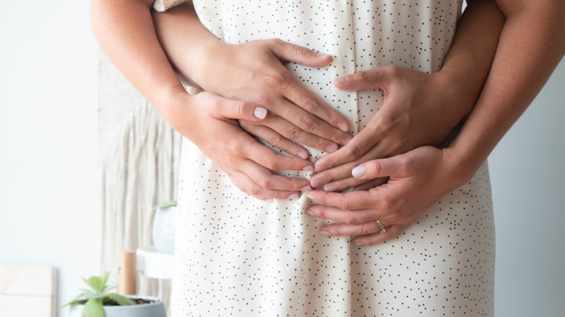 a couple standing while keeping their hands on the stomach of the soon-to-be mom