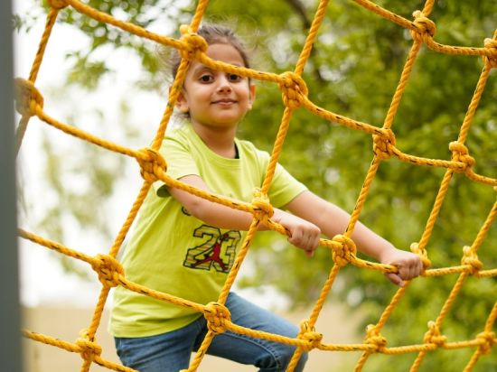 Kid on a commando net ride at inflated trampoline surrounded by trees at Themis Mudhouse - A Nature's Retreat Resort & Wellness