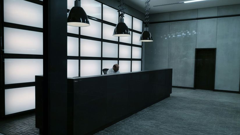 a receptionist sitting behind a reception desk in an office building with lights hanging above his head