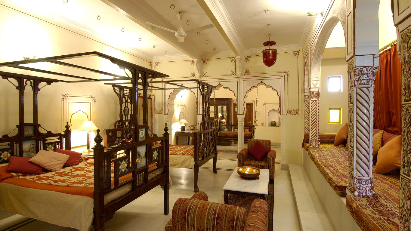 a brightly lit room with a two large beds with a canopy and sofas for sitting - Hotel Castle Mandawa, Jhunjunu