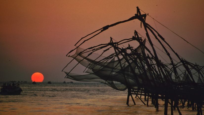 Fishes nets being pulled up with the sun setting in the background in the backwaters kochi