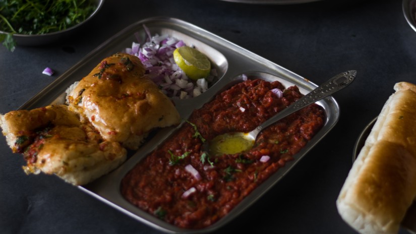 a platter of pav bhaji with onions and a lemon and a spoonful of butter garnished with coriander leaves