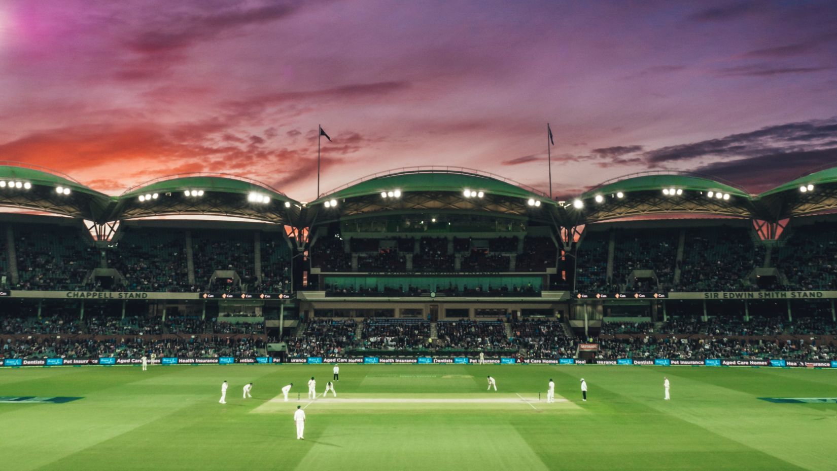 an image of a stadium with people playing cricket during dusk