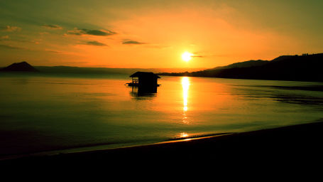  A serene sunset over a calm lake, with the sun's reflection on the water and a solitary boat creating a tranquil silhouette against the golden sky.