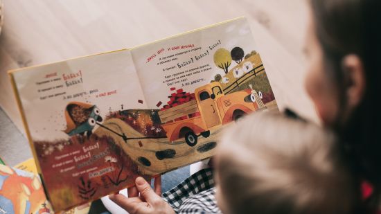 A lady holding a colourful storybook and narrating the story to the child 