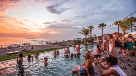 a crowd of people enjoying by dipping into the pool and looking at the sunset in the background