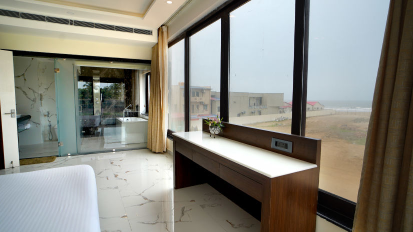 a table in front of floor to ceiling windows and a double bed opposite to it inside one of the rooms - Shanti Seaview Resort & Spa