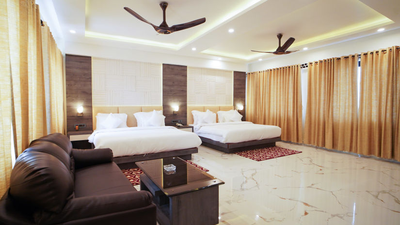 A twin double bed with pillows on it and a sofa with a coffee table in the foreground inside one of the rooms at Shanti Seaview Resort & Spa - Mandarmani Hotels near Beach with Swimming Pool