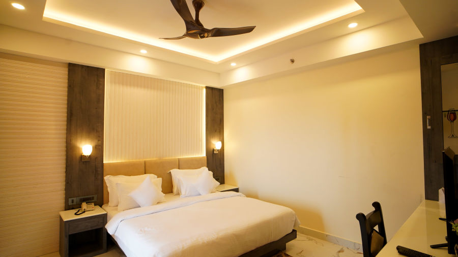 a double bed with side tables and lamps on it and a study table opposite the bed inside one of the rooms - two seats with a small table in one of the balcony with view of an empty land inside one of the rooms - Shanti Seaview Resort & Spa