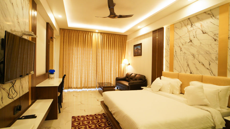 a double bed with a sofa on one side and a tv wall mounted opposite the bed in one of the rooms - Shanti Seaview Resort & Spa