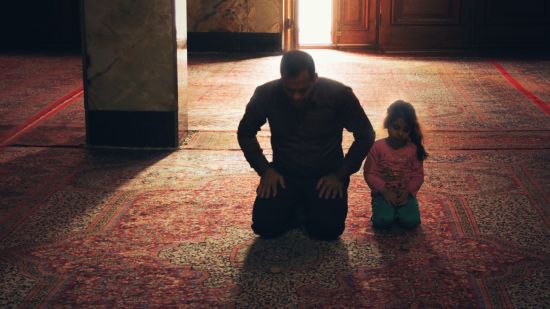 a person with their child praying inside a room with the sun light showing from the door