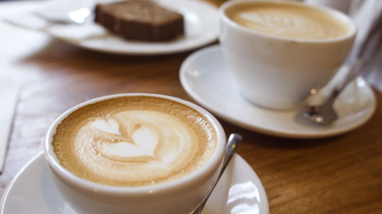 a close up shot of Coffees on a table with a slice of bread in the background - La Maison Hotel, Doha