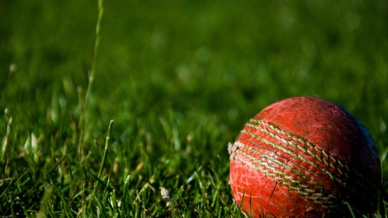 a close up shot of a red cricket ball on the grass 