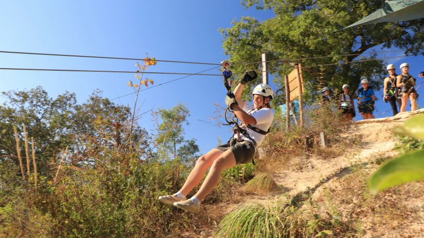 A boy ziplining on top of a lush green hillside