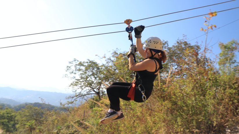 a woman ziplining downward with the sky and hills in the background