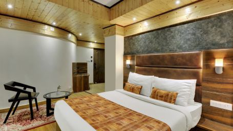 Deluxe bedroom with a large bed and chairs with false ceiling lighting and side lamps - Sumi Queensyard, Darjeeling