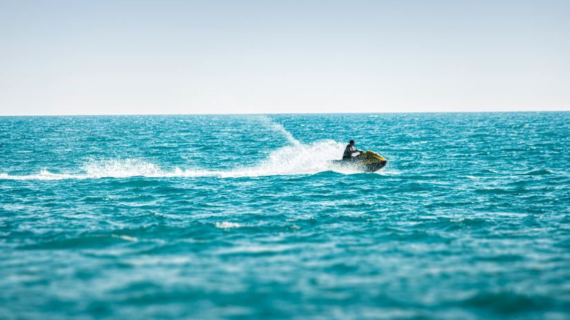 View  of an individual enjoying Jet Ski in the ocean, deep blue colour of the ocean glistening under sunlight 