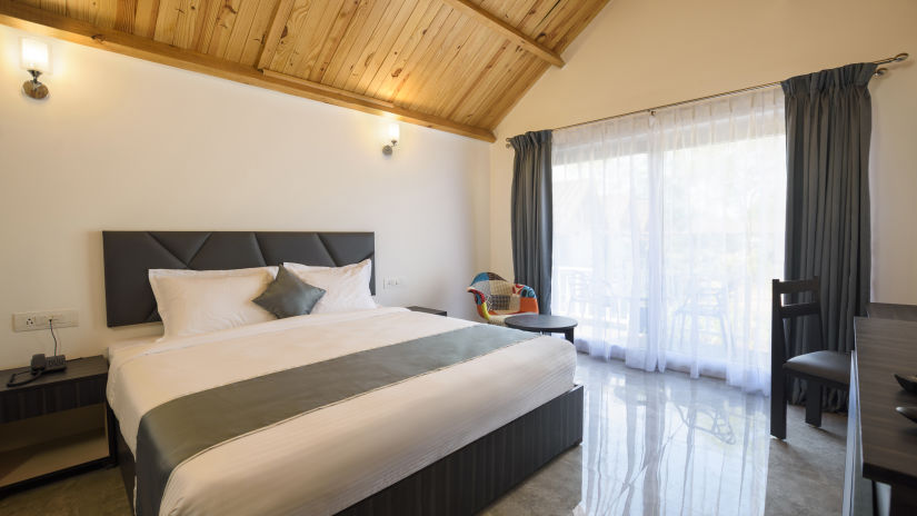 The pool front cottage room features a large bed, a balcony and  a gable roof - White Woods Resort, Morjim