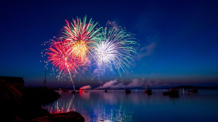 fireworks lighting up the night sky with different colours as seen from the shore of a river