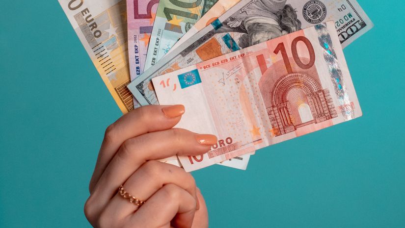 a person holding currencies of different countries with a green painted wall in the background