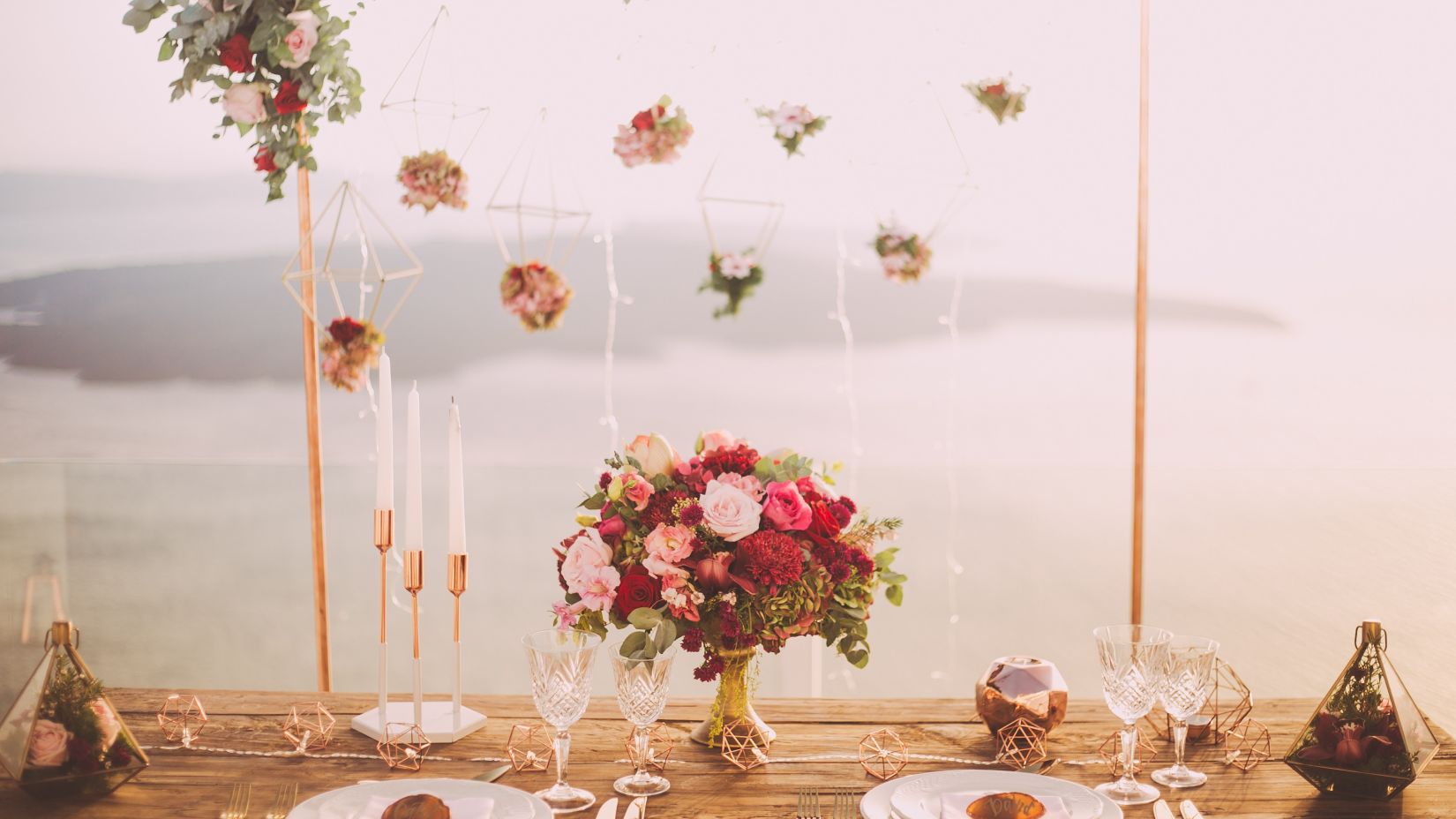 a table for two with cutlery, a bouquet of flowers and decorations on it with a lake in the background