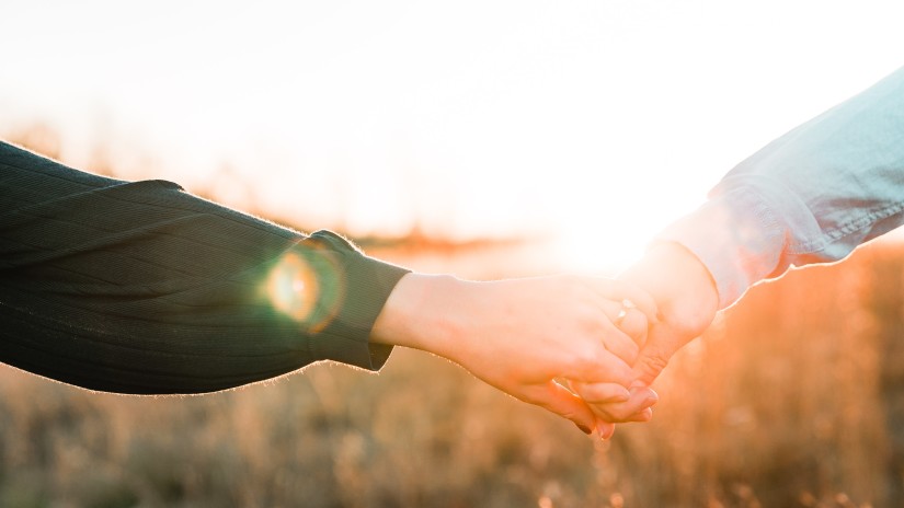 a close up image of a Couple holding hands with the sun just above their hands