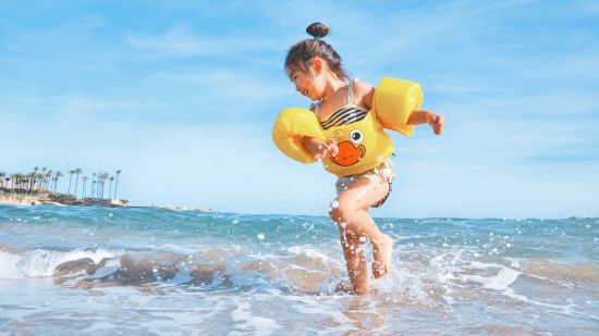 A young girl in a yellow swim vest runs away from the gentle shore waves - Varca Beach Stay