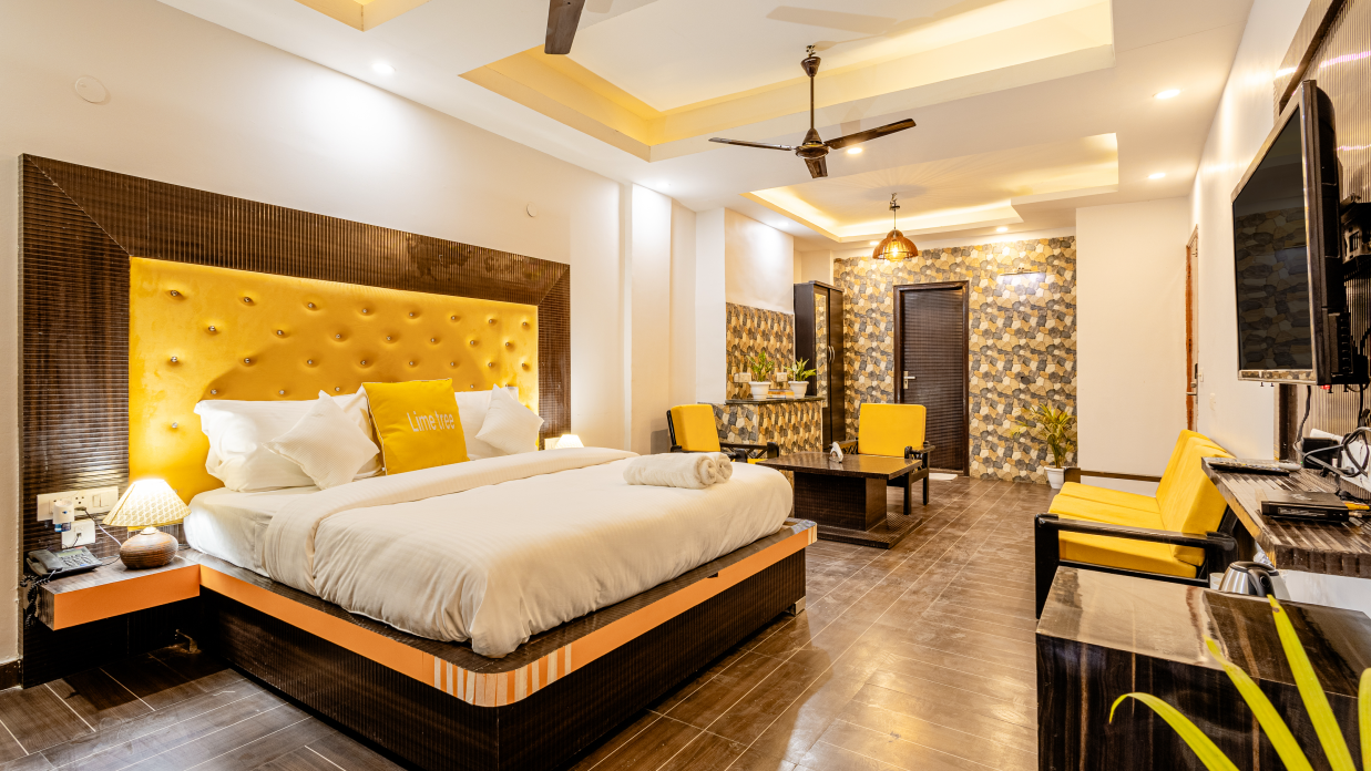 side view of the king size bed, the living area and a television in the suite at Lime Tree Hotels and Banquet Hall Near Huda Metro, Gurgaon