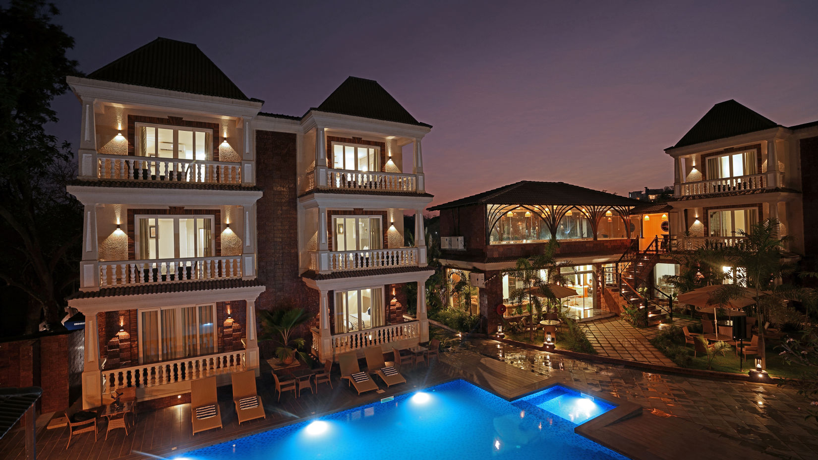 Illuminated building by night with a glowing pool in the foreground - Grand Continent, Anjuna - A Sarovar Portico Affiliate Hotel 