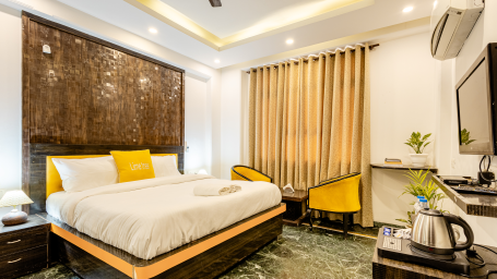 Side and wide angle view of the king size bed, two chairs and a television in the superior king room at Lime Tree Hotels and Banquet Hall Near Huda Metro, Gurgaon