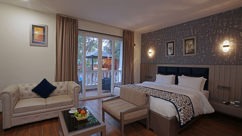 Corner view of the room with cosy bed and sofa and tea table have a window with view of the flavour restaurant - Grand Continent, Anjuna - A Sarovar Portico Affiliate Hotel  