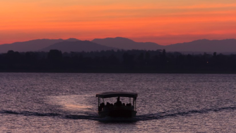 a boat travelling on a waterbody with the sky having different hues after a sunset