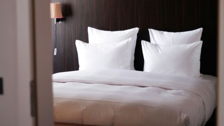 a view of a room featuring a white bed with fluffy cushions