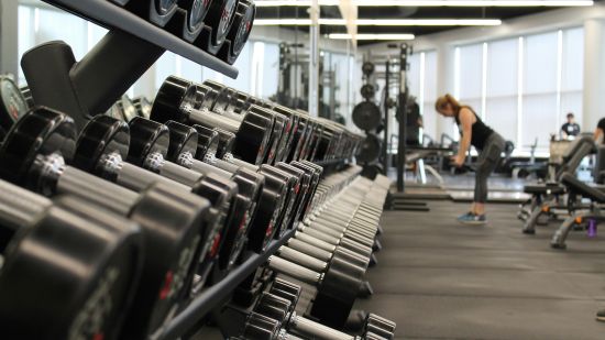 A close up shot of dumbbells in a rack with a person in the background working out