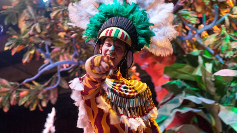 a man dress in fancy tribal clothing dressed up for a fiesta and pointing at the camera