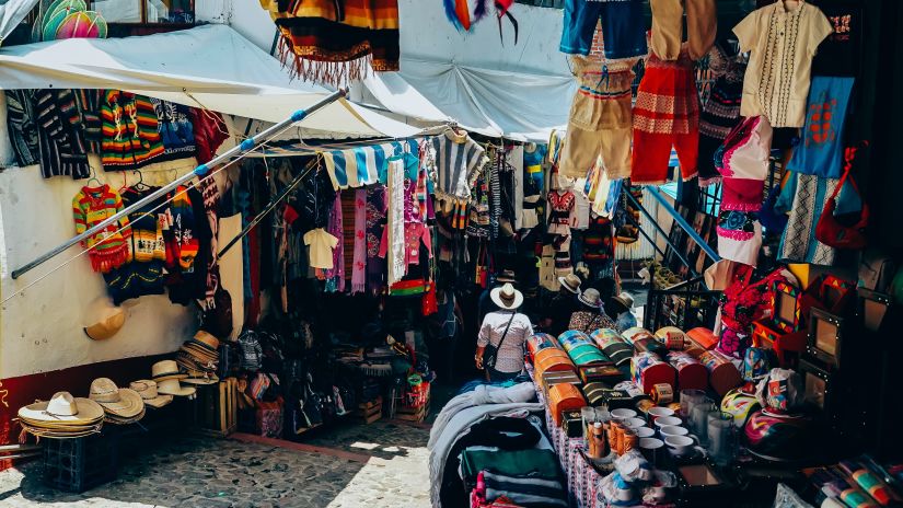 A person walking in a colourful street market with clothes shops around