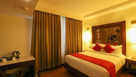 A clean room with a tidy bed, curtains, and table - The Saibaba Hotel