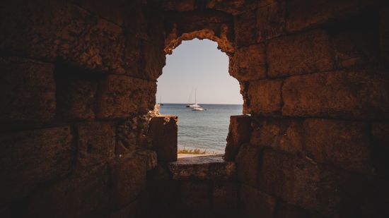 beautiful-shot-sea-with-sailboats-from-inside-hole-stone-wall