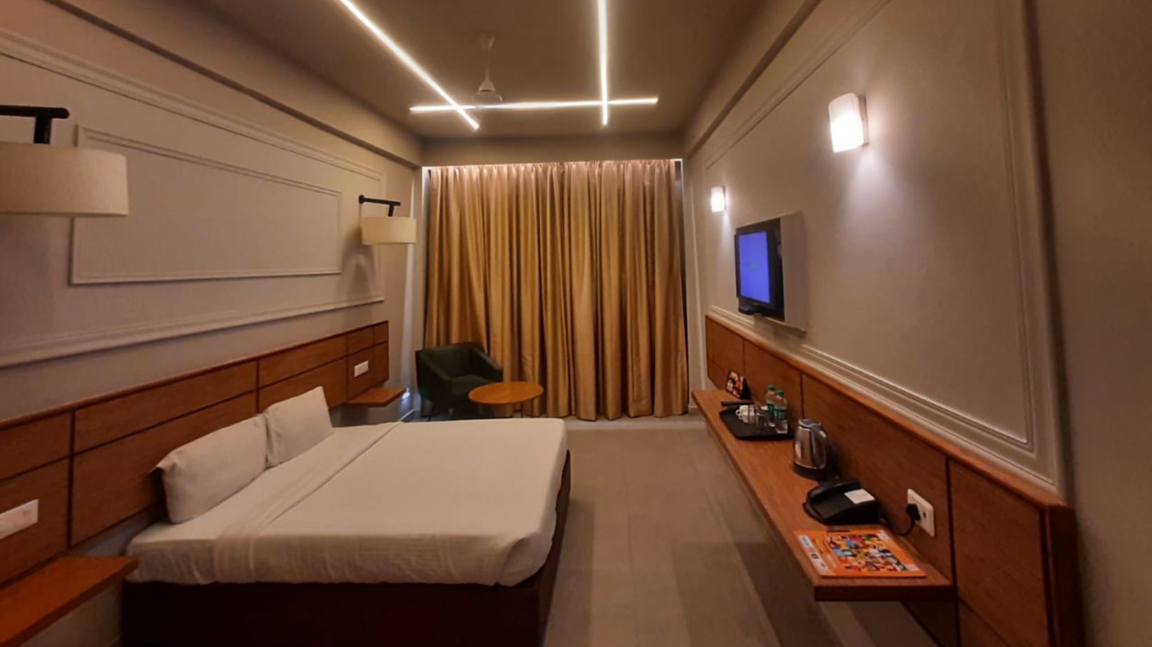 A  side view of a spacious room with a plushy bed and flat screen TV at Max Hotel Prayagraj